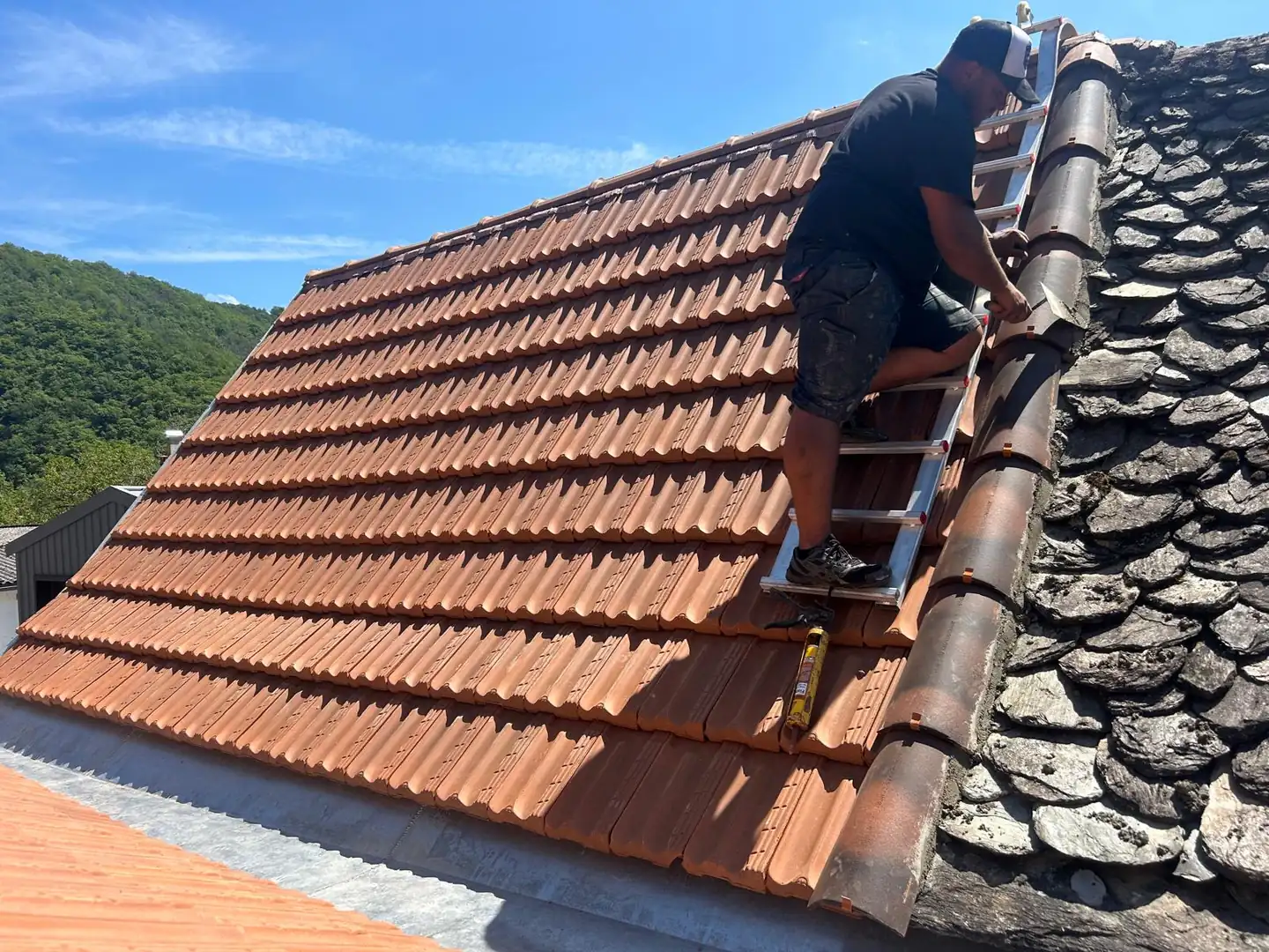 Artisan couvreur posant une tuile faîtière sur un toit en rénovation